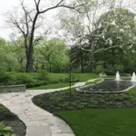 a stone walkway with a fountain in the middle of a park